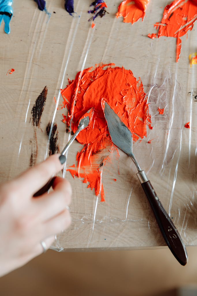 A close-up of vibrant acrylic paint being mixed with a palette knife on a table.