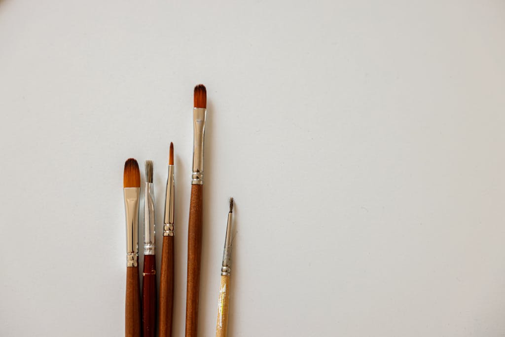 A collection of five paint brushes laid on a clean white surface, ideal for artistic purposes.