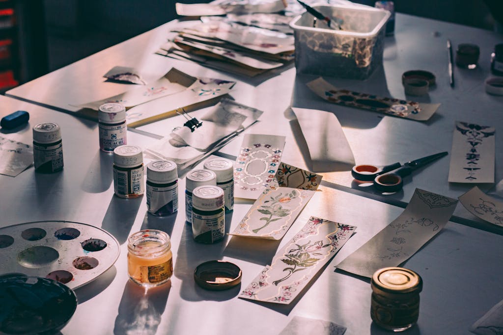 A creative workspace with paints, brushes, and decorative paper designs in a sunlit studio.