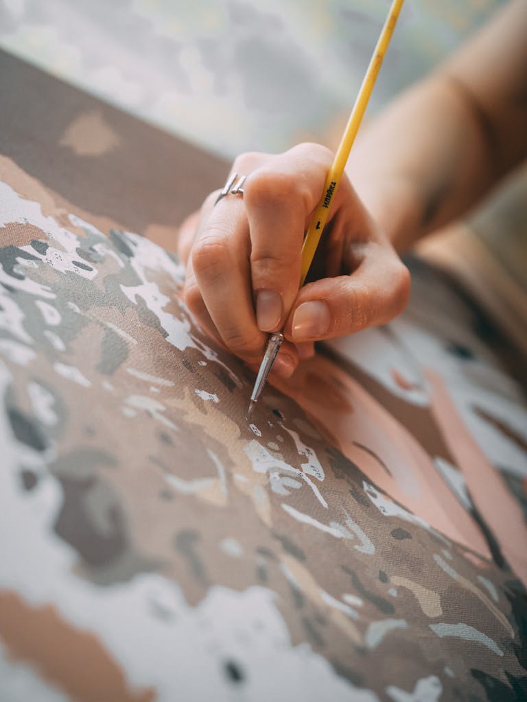 A detailed view of a hand carefully painting on a canvas, showcasing artistic creativity and technique.