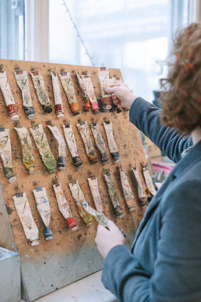 A focused artist selects paint tubes from a well-used board in a creative studio setting.