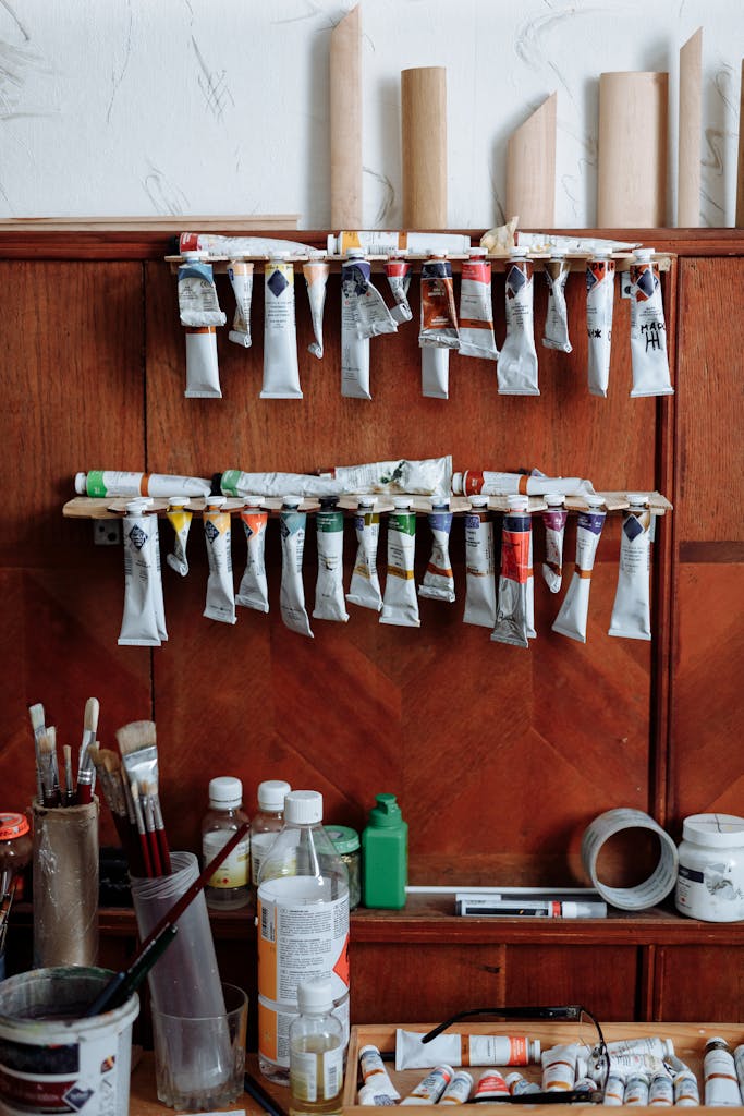 A vibrant collection of paint tubes and brushes organized on a wooden shelf in an art studio.