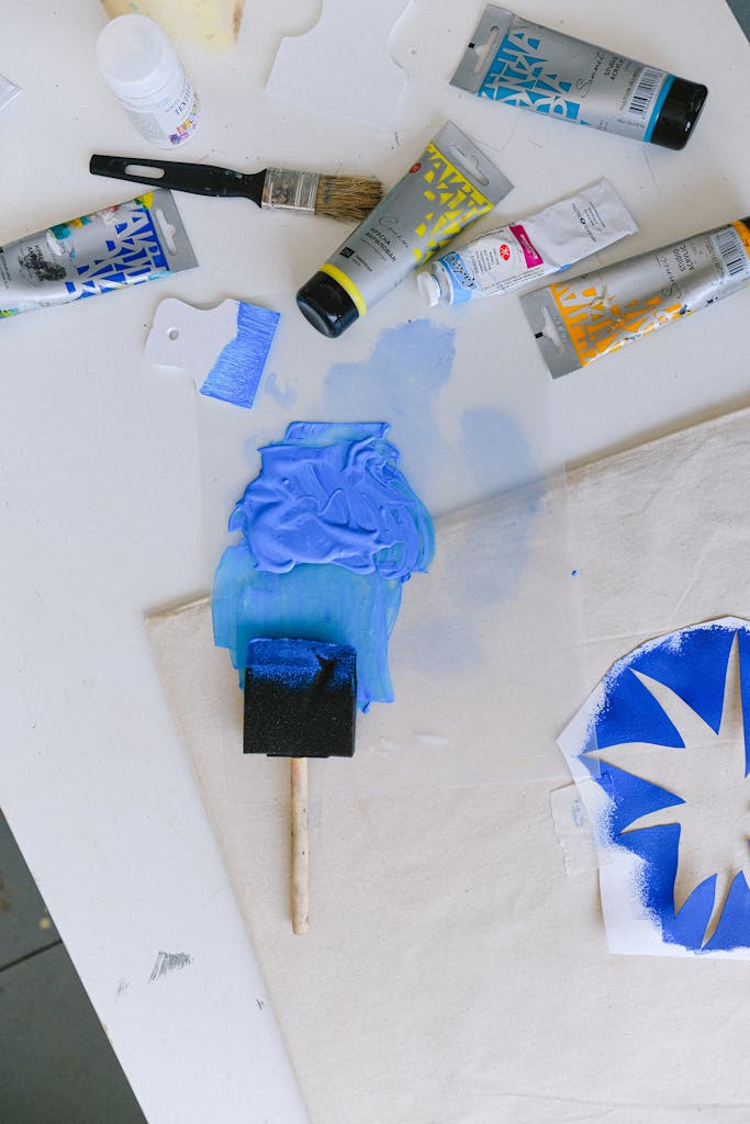 A vibrant workspace showcasing blue paint, brushes, stencils, and tools for artistic creation indoors.