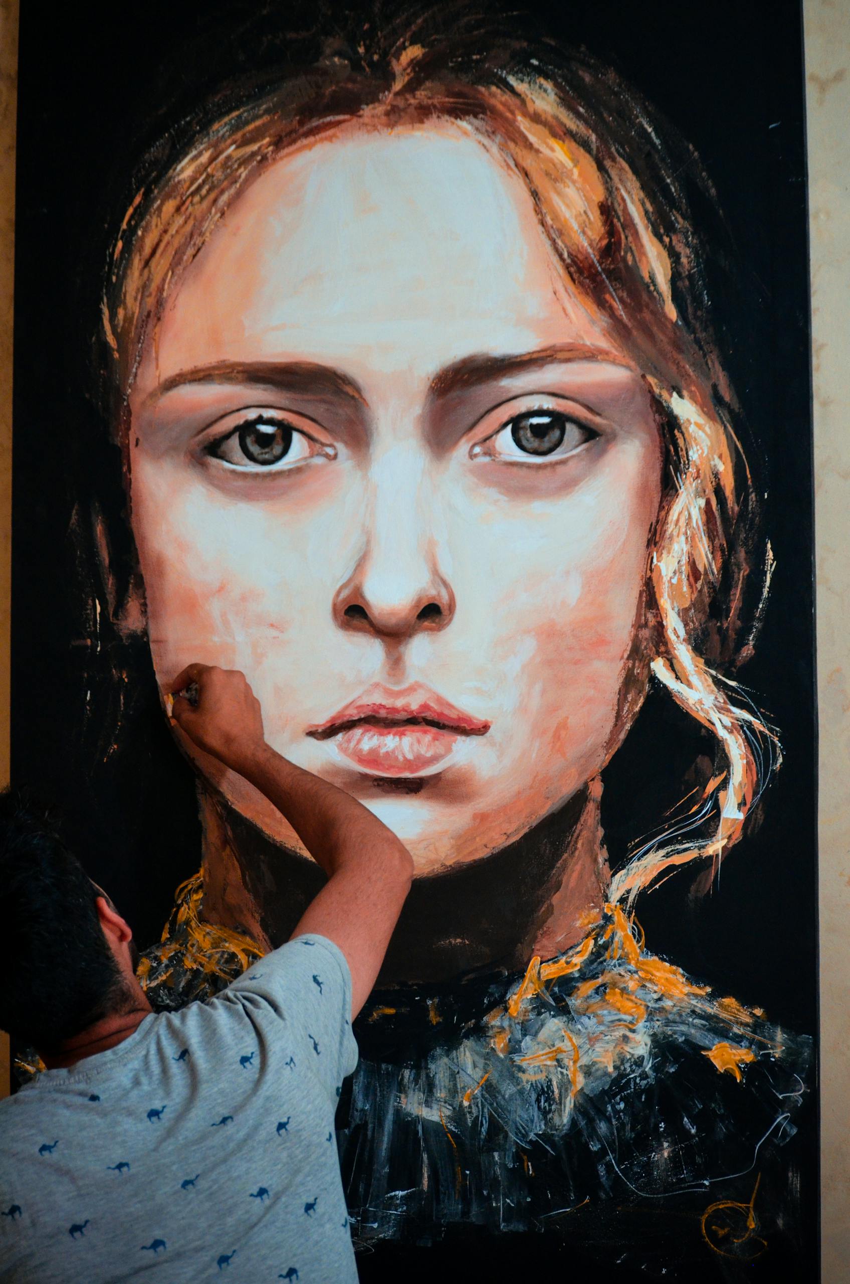 An artist meticulously paints a large portrait of a woman on canvas in an indoor art studio.