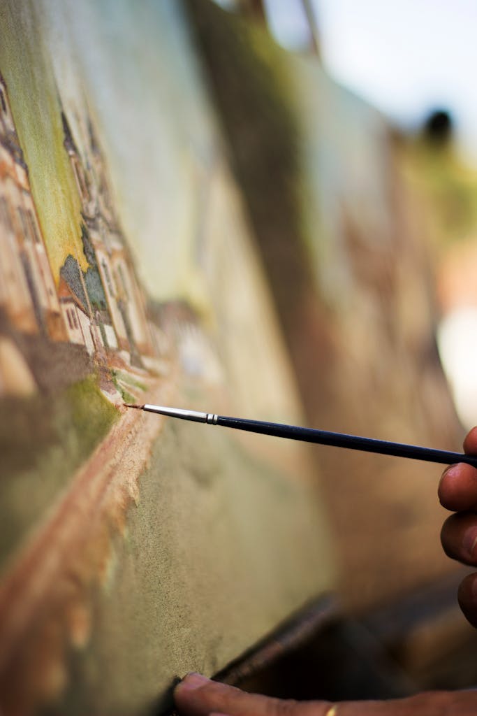 An artist's hand skillfully paints on a canvas outdoors, capturing a vibrant scenery.