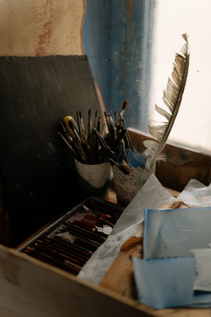 Artistic workspace featuring paintbrushes, feather, paper, and art supplies on a wooden table.
