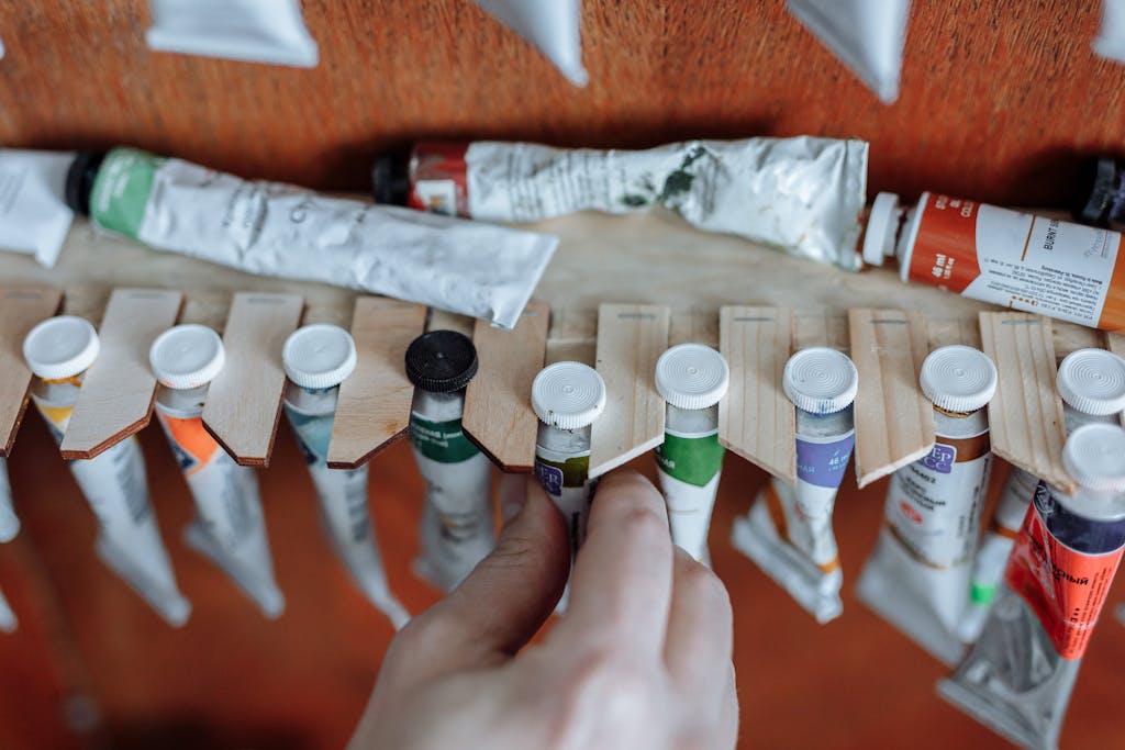 Artist's hand selecting a paint tube from a wooden organizer with various acrylic colors.