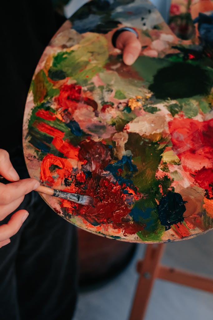 Close-up of a hand holding a vibrant paint palette and brush in use.