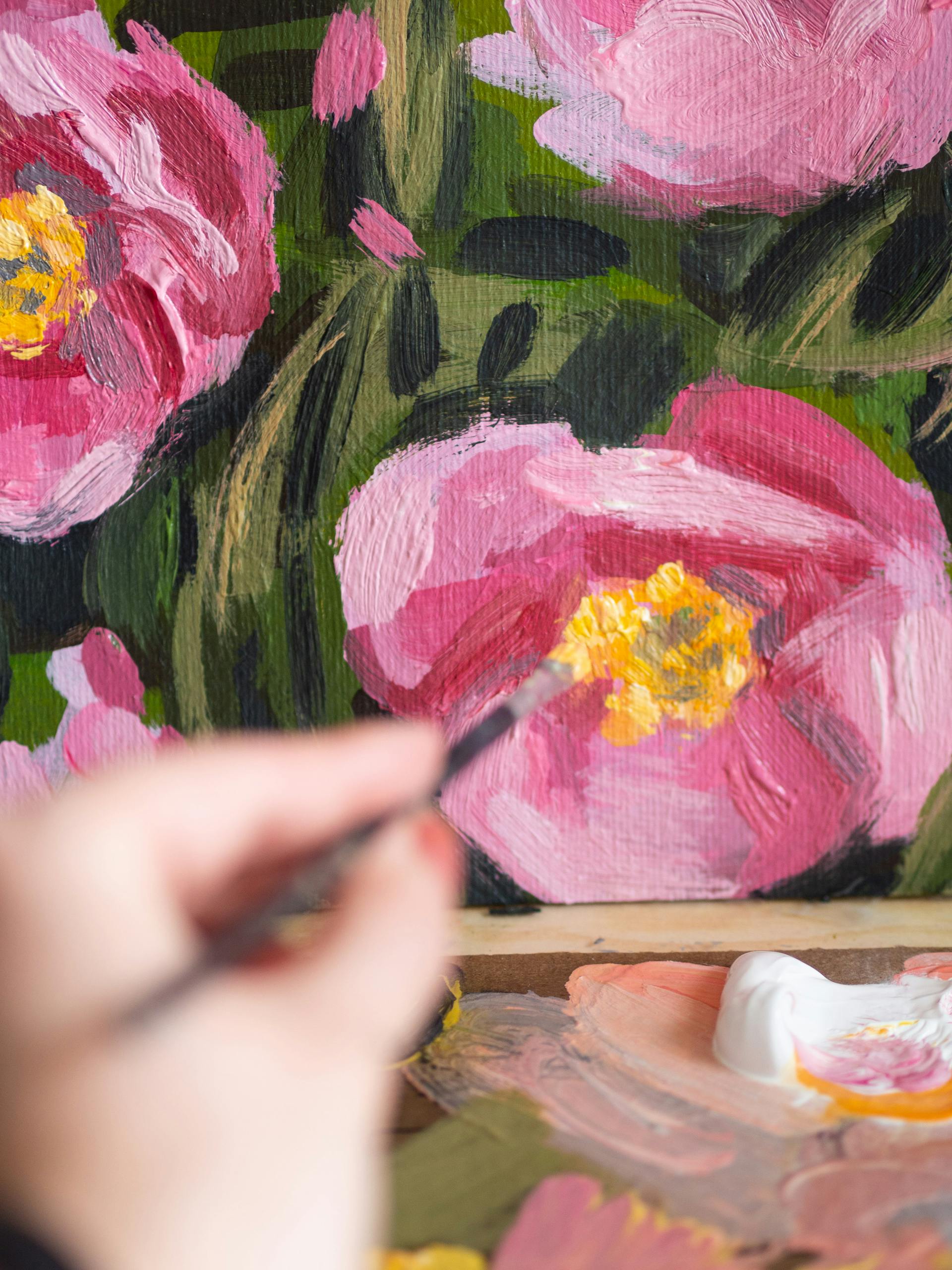 Close-up of a hand painting pink flowers on canvas, showcasing artistic brush strokes and vivid colors.
