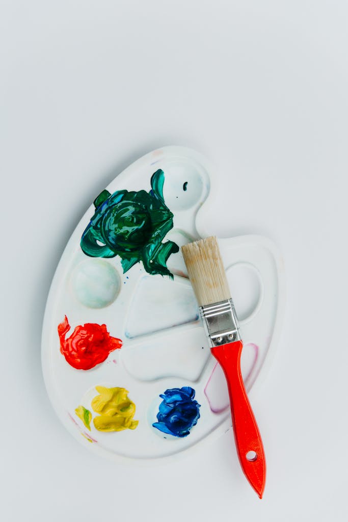 Close-up of a vibrant paint palette with a red-handled brush for creative projects.