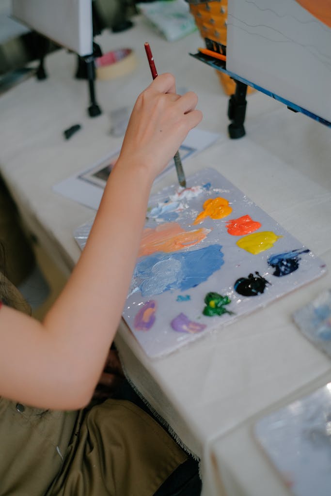 Close-up of an artist's hand painting with a colorful palette on a table.