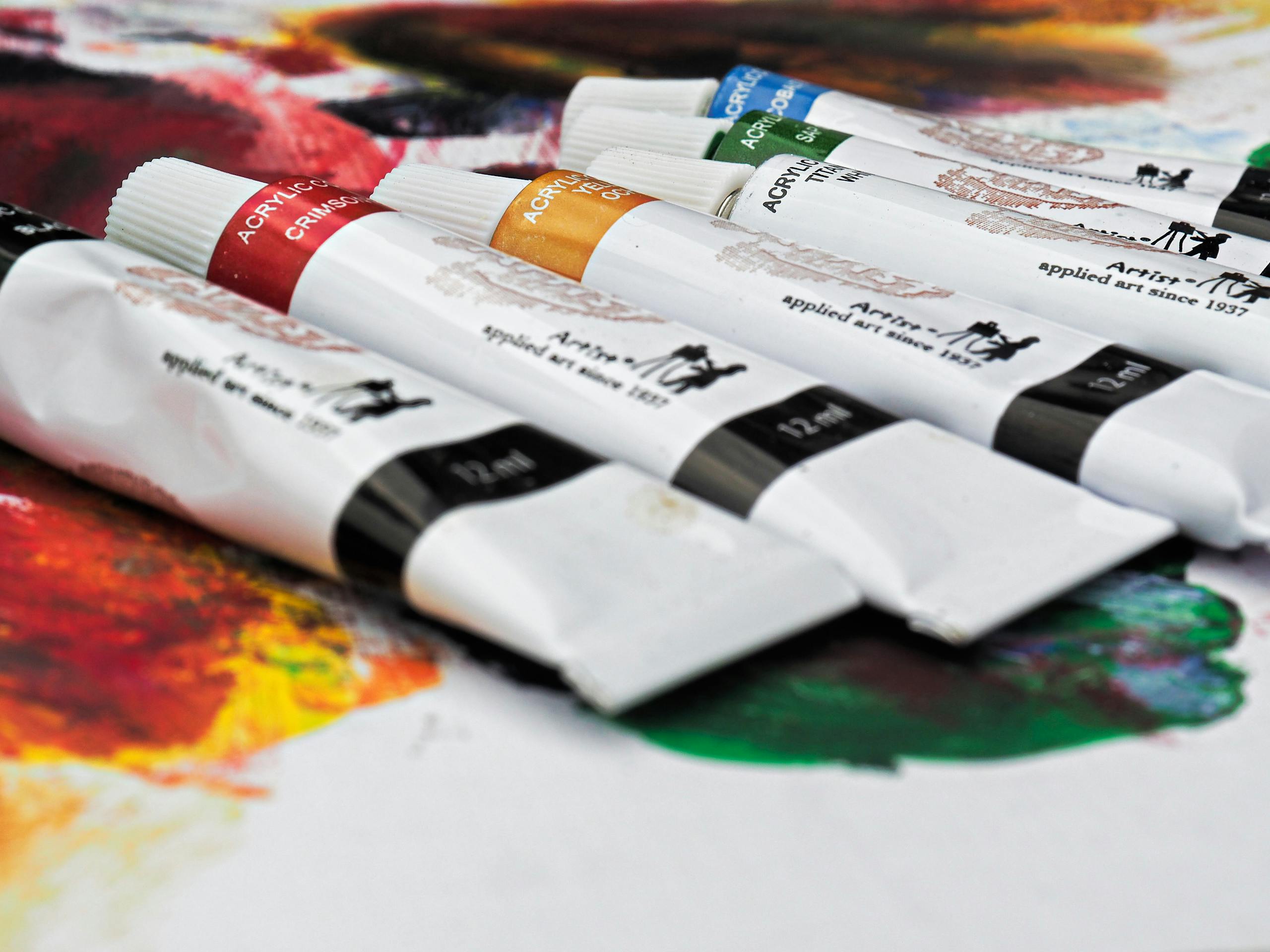 Close-up of assorted acrylic paint tubes on a colorful canvas ready for creativity.