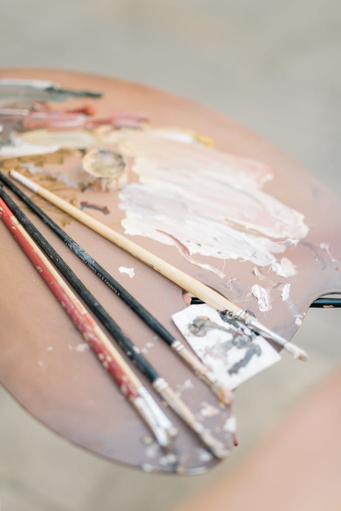 Close-up of paint brushes resting on a wooden palette with mixed colors.