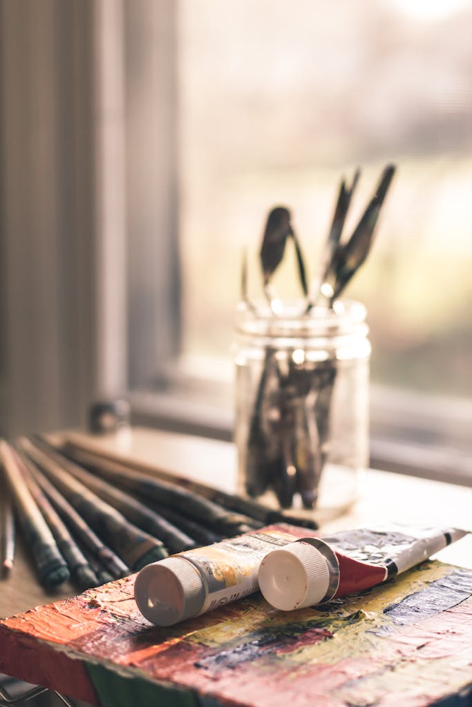Close-up of paint tubes and brushes on a table by the window in warm lighting. Perfect for creative themes.