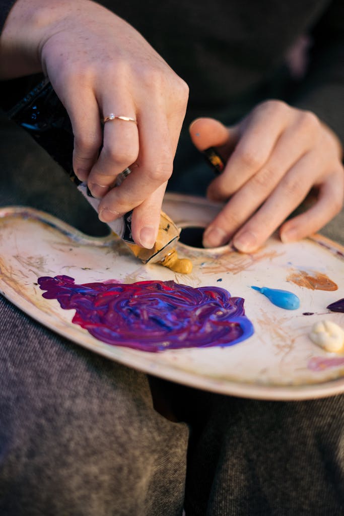 Hands squeezing acrylic paint onto a painter's palette, showcasing creativity and vibrant colors.