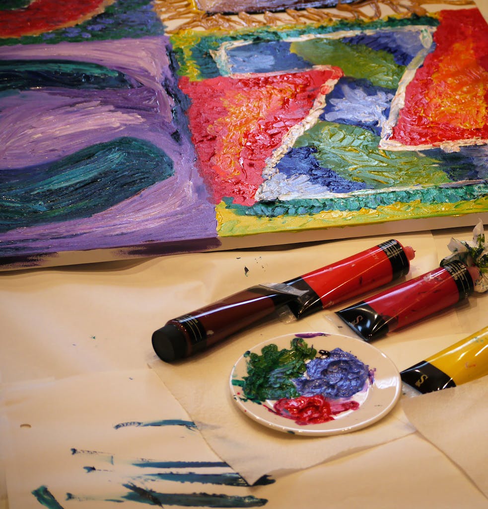 Vibrant abstract artwork with paint tubes and a palette in a creative setup.
