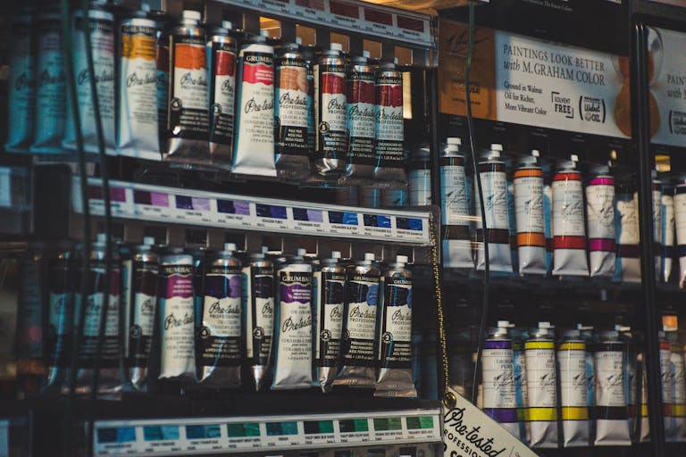 Vibrant art store aisle featuring a row of colorful professional paint tubes on display shelves.