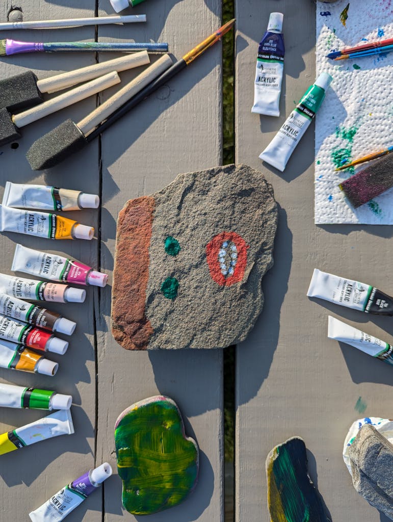 Vibrant rock painting with acrylics and tools on a wooden table.